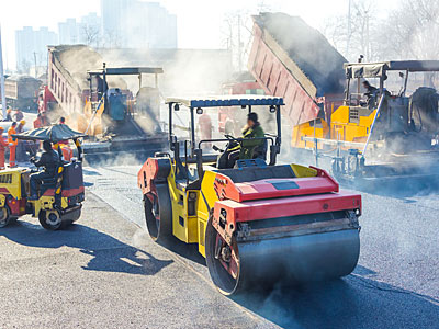 Baustelle mit Walze und Lkw, die Asphalt liefern.